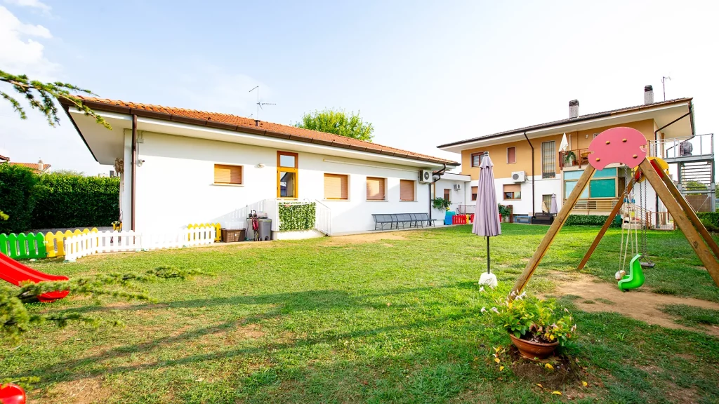 Il giardino della struttura, ampio e con molti giochi a disposizione dei bambini. Si vede anche la struttura esterna dell'asilo nido. 